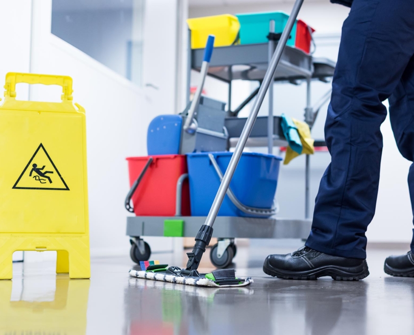 Front view of a custodian mopping the floor with a wet floor sign in the frame