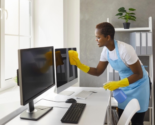 Professional janitor cleaning office desk and computer